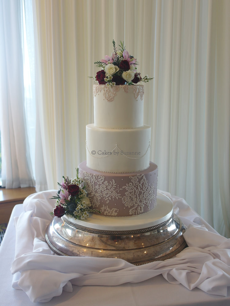 three tier round stacked wedding cake with sugar lace and pearls decorated with fresh flowers