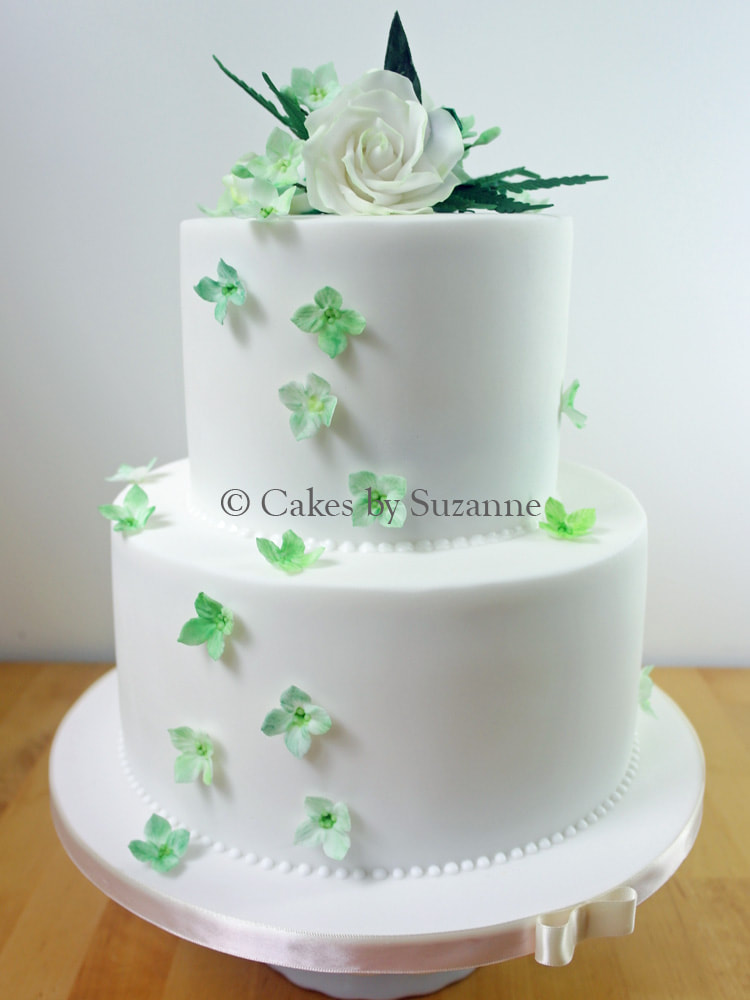 two tier round wedding cake with white and green roses and blossoms