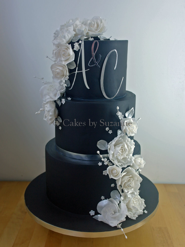 black three tier round stacked wedding cake with white sugar flowers and silver initials