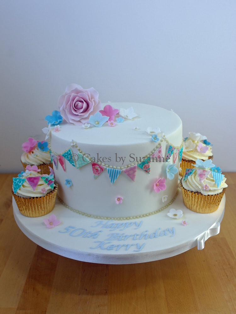 50th birthday cake with pastel sugar roses, blossom and bunting and matching cupcakes displayed on board