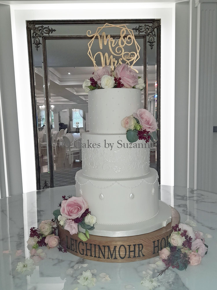 three tier round wedding cake with sugar pearls and lace, decorated with fresh flowers