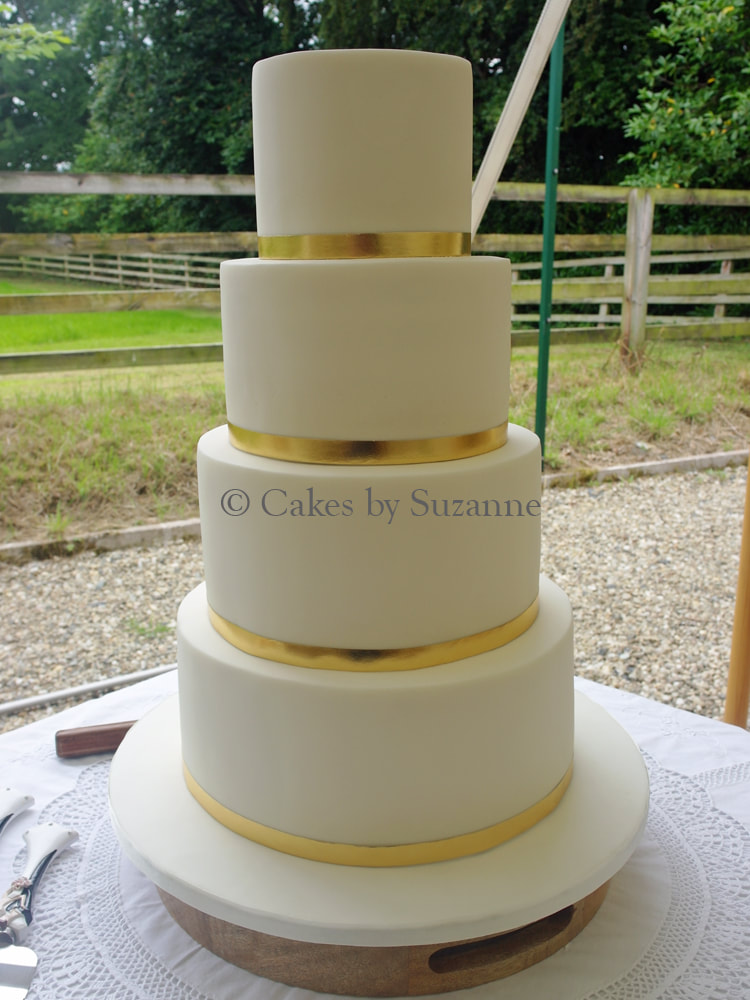 four tier round stacked wedding cake with simple gold trim, ready to be decorated with fresh flowers