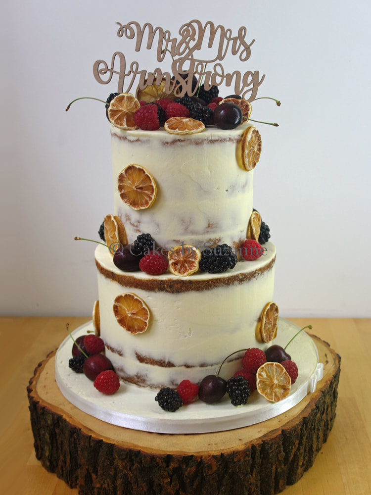 two tier round stacked semi naked buttercream wedding cake with fresh raspberries, blackberries, cherries and dried lemon slices