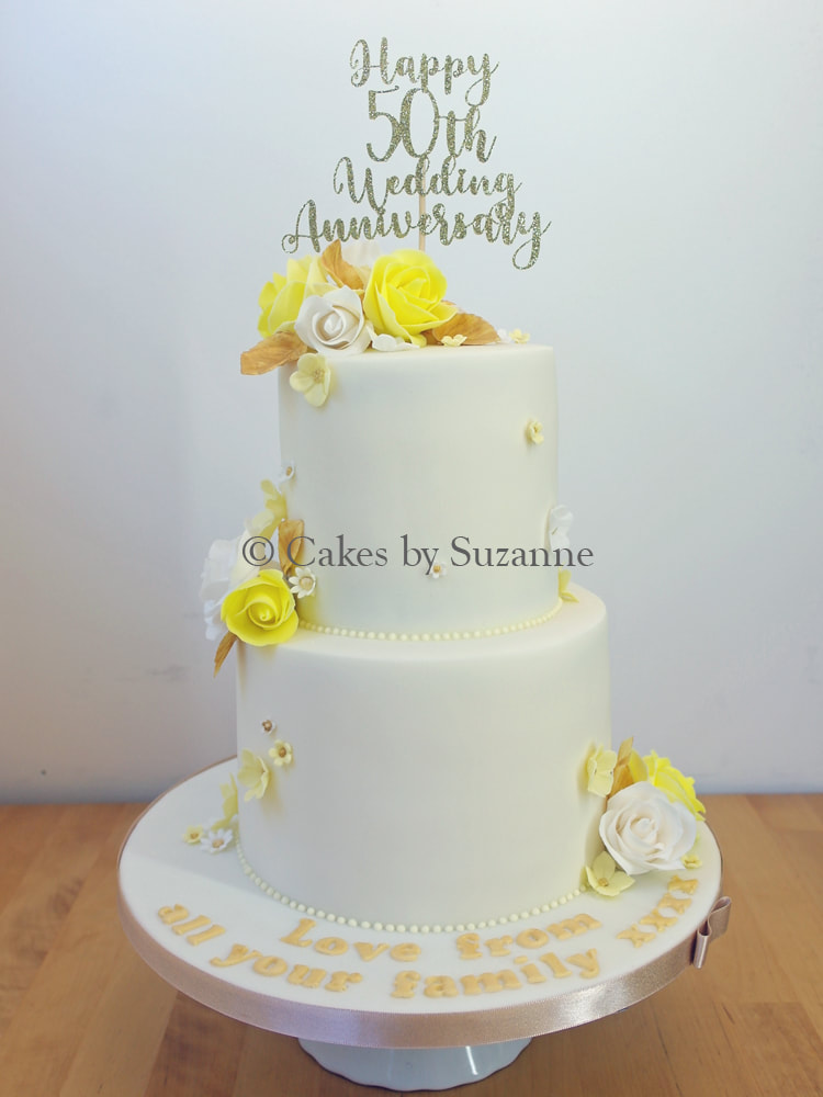 two tier round stacked 50th golden wedding anniversary cake with yellow and gold roses and blossoms and personalised anniversary topper