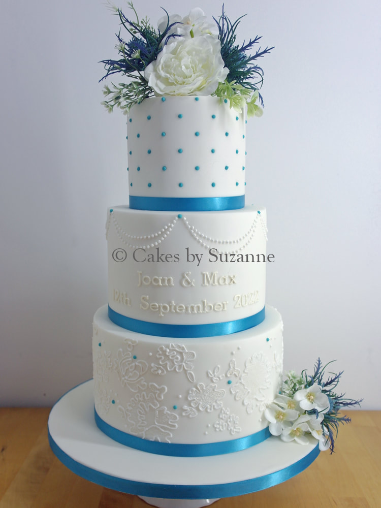 three tier round stacked wedding cake with teal ribbon and silk flowers